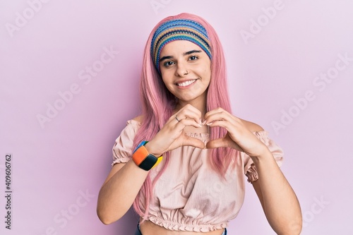 Young hispanic girl with pink hair smiling in love doing heart symbol shape with hands. romantic concept.