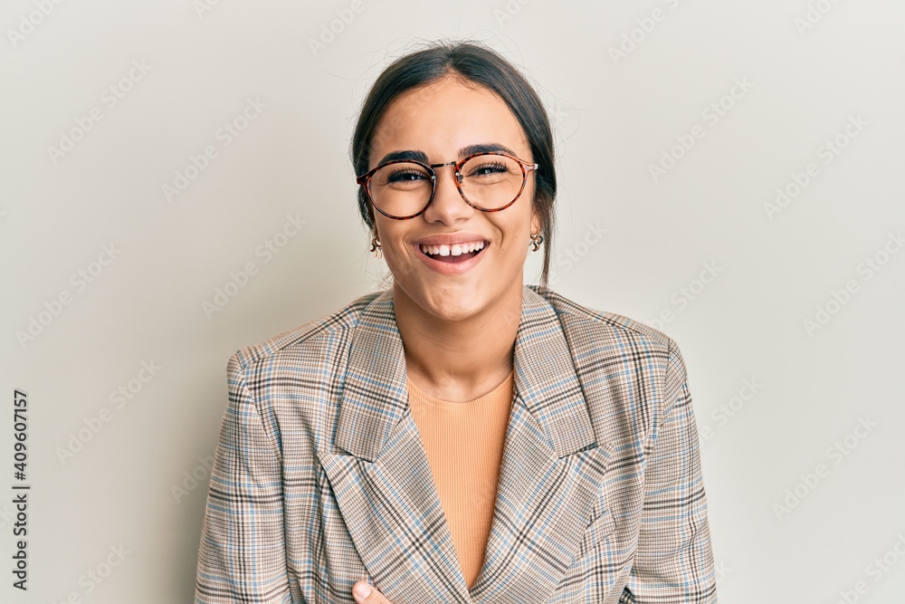 Young brunette woman wearing business jacket and glasses smiling and laughing hard out loud because funny crazy joke with hands on body. Young brunette woman wearing business jacket and glasses smiling and laughing hard out loud because funny crazy joke with hands on body.