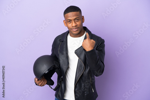 Latin man with a motorcycle helmet isolated on purple background doing coming gesture