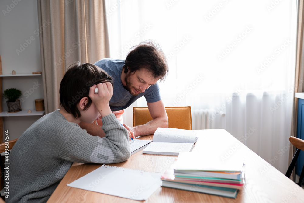 Teenager boy doing school lessons at home. Dad helping solve difficult math problems. Problems and difficulties of home education Teenager boy doing school lessons at home. Dad helping solve difficult math problems. Problems and difficulties of home education