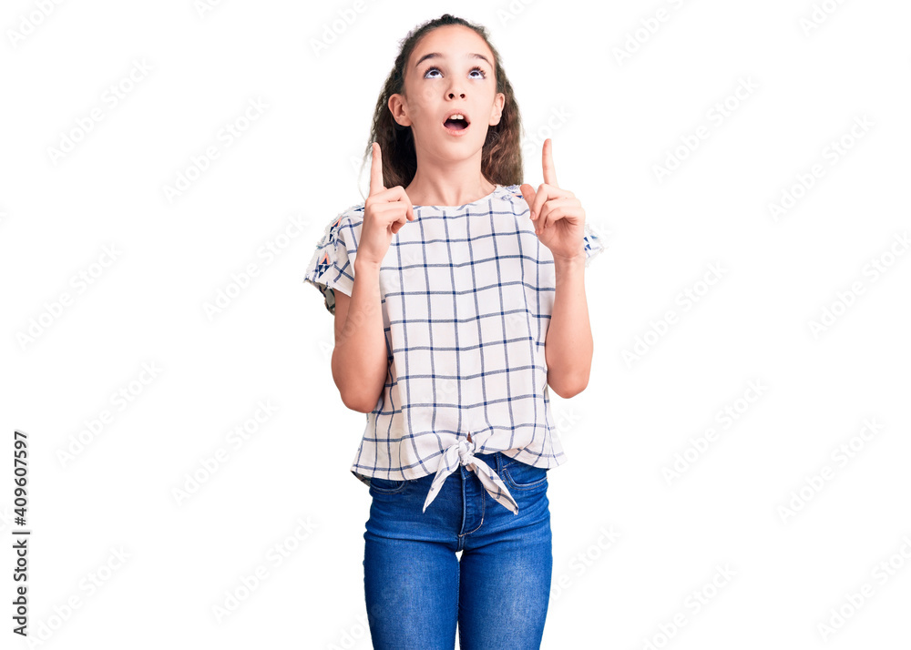 Cute hispanic child girl wearing casual clothes amazed and surprised looking up and pointing with fingers and raised arms. Cute hispanic child girl wearing casual clothes amazed and surprised looking up and pointing with fingers and raised arms.
