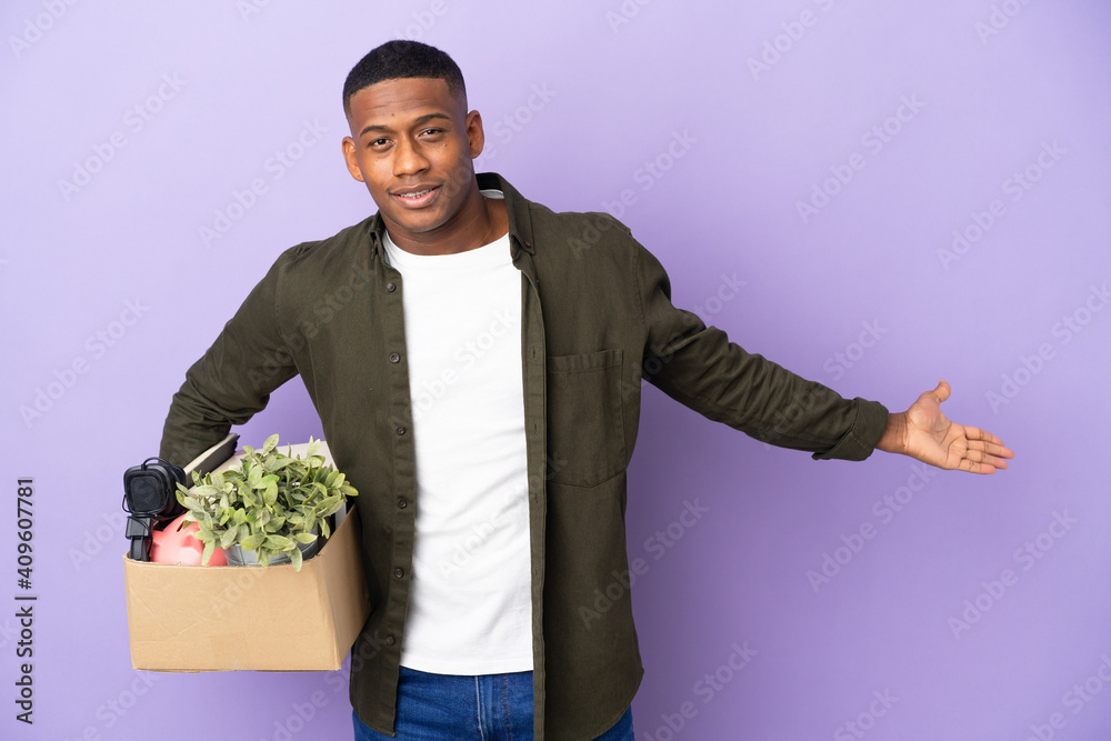 Latin man making a move while picking up a box full of things extending hands to the side for inviting to come Latin man making a move while picking up a box full of things extending hands to the side for inviting to come