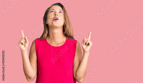 Middle age hispanic woman wearing casual clothes amazed and surprised looking up and pointing with fingers and raised arms.