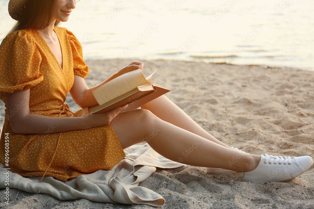 Young woman reading book on sandy beach near sea, closeup