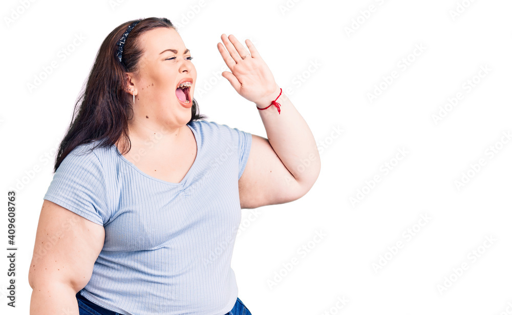 Young plus size woman wearing casual clothes shouting and screaming loud to side with hand on mouth. communication concept. Young plus size woman wearing casual clothes shouting and screaming loud to side with hand on mouth. communication concept.