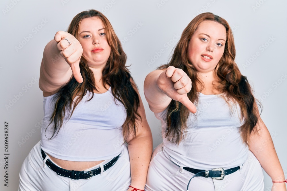 Plus size caucasian sisters woman wearing casual white clothes looking unhappy and angry showing rejection and negative with thumbs down gesture. bad expression. Plus size caucasian sisters woman wearing casual white clothes looking unhappy and angry showing rejection and negative with thumbs down gesture. bad expression.