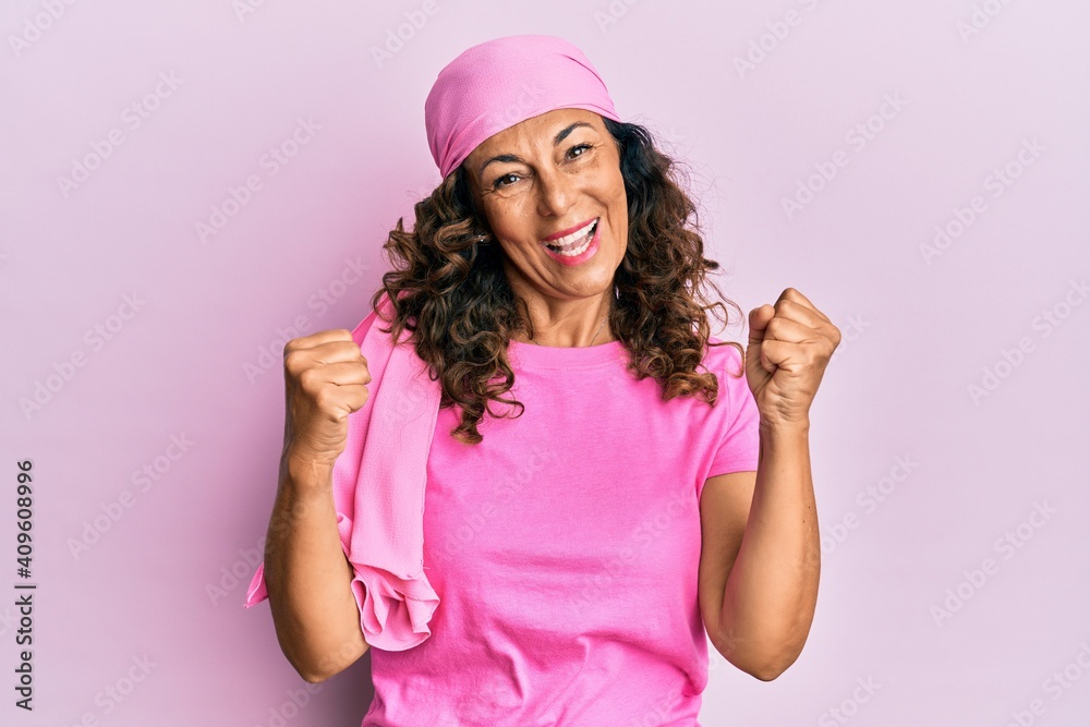 Middle age hispanic woman wearing breast cancer support pink scarf screaming proud, celebrating victory and success very excited with raised arms Middle age hispanic woman wearing breast cancer support pink scarf screaming proud, celebrating victory and success very excited with raised arms
