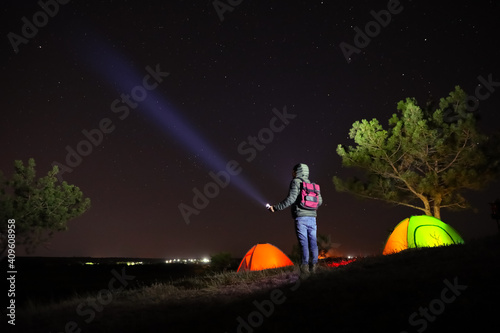 Man with bright flashlight near camping tents outdoors at night