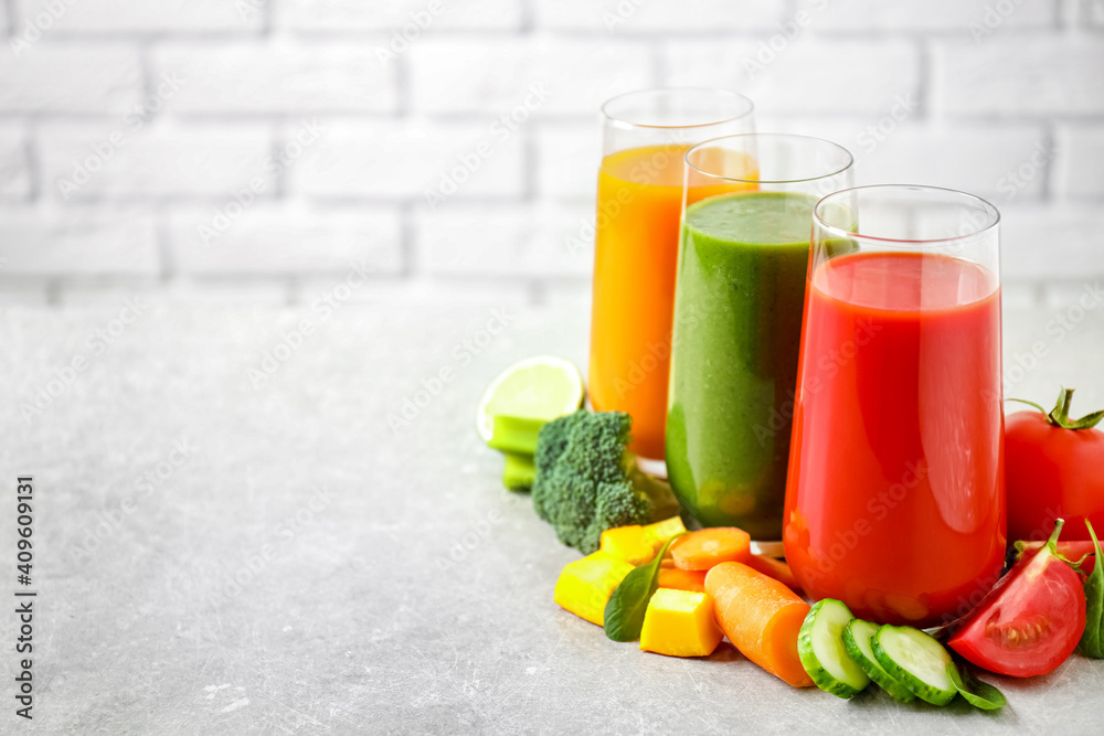 Different tasty juices and fresh ingredients on grey table against brick wall. Space for text Different tasty juices and fresh ingredients on grey table against brick wall. Space for text