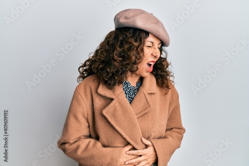 Middle age hispanic woman wearing french look with beret with hand on stomach because nausea, painful disease feeling unwell. ache concept.