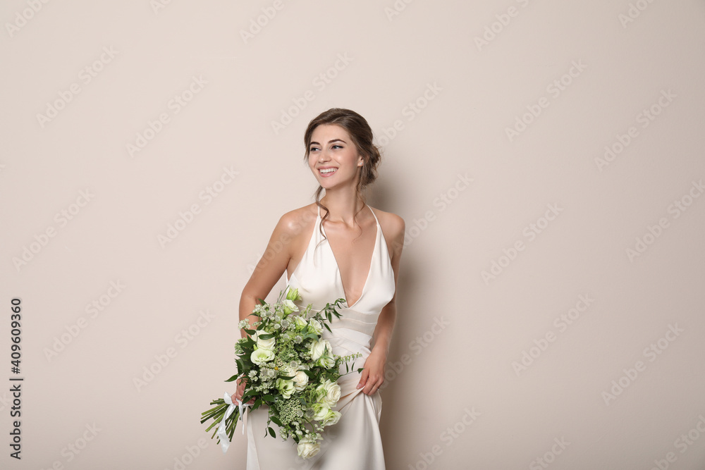 Young bride wearing wedding dress with beautiful bouquet on beige background Young bride wearing wedding dress with beautiful bouquet on beige background