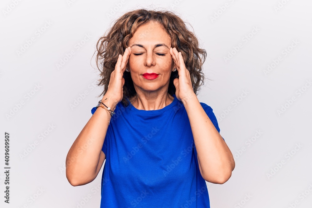Middle age beautiful brunette woman wearing blue t-shirt standing over white background with hand on head, headache because stress. Suffering migraine. Middle age beautiful brunette woman wearing blue t-shirt standing over white background with hand on head, headache because stress. Suffering migraine.