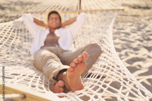 Man relaxing in hammock outdoors, focus on legs © New Africa