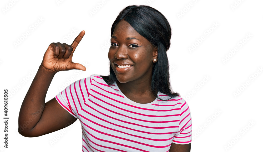 African young woman wearing casual striped t shirt smiling and confident gesturing with hand doing small size sign with fingers looking and the camera. measure concept. African young woman wearing casual striped t shirt smiling and confident gesturing with hand doing small size sign with fingers looking and the camera. measure concept.