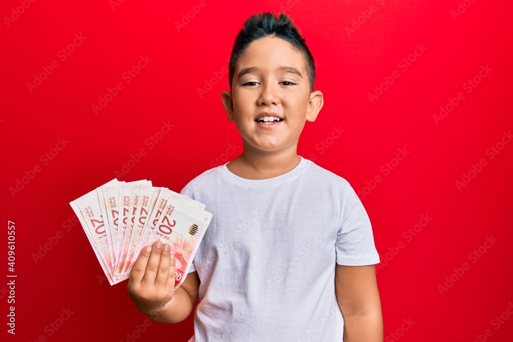 Little boy hispanic kid holding 20 israel shekels banknotes looking positive and happy standing and smiling with a confident smile showing teeth Little boy hispanic kid holding 20 israel shekels banknotes looking positive and happy standing and smiling with a confident smile showing teeth