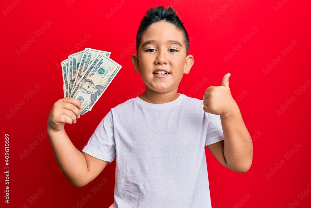 Little boy hispanic kid holding 20 dollars banknotes smiling happy and positive, thumb up doing excellent and approval sign Little boy hispanic kid holding 20 dollars banknotes smiling happy and positive, thumb up doing excellent and approval sign