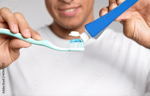 Man applying toothpaste on brush against light background, closeup