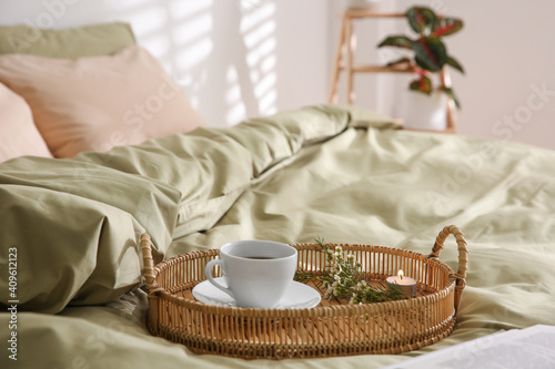 Tray with cup of coffee, candle and flowers on soft olive blanket indoors