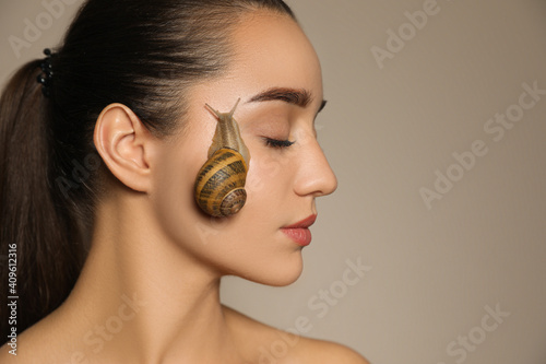 Beautiful young woman with snail on her face against beige background. Space for text photo