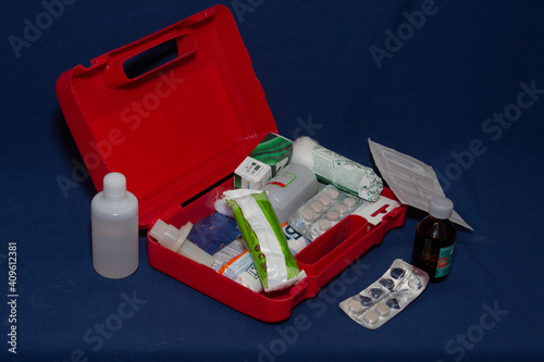 Plastic red first aid kit with medicines on blue background 