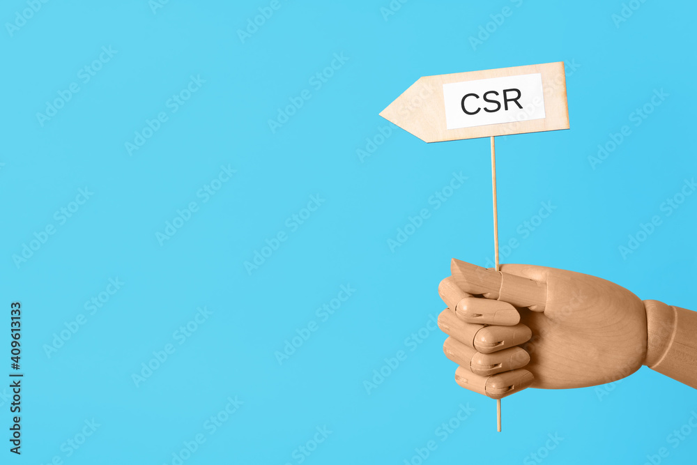 Wooden mannequin holding sign with abbreviation CSR on light blue background, closeup. Corporate social responsibility Wooden mannequin holding sign with abbreviation CSR on light blue background, closeup. Corporate social responsibility