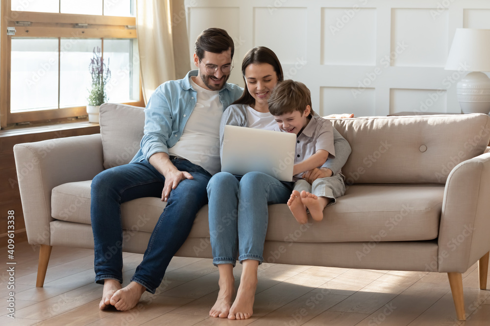 Overjoyed young Caucasian family with little 7s son sit relax on sofa watch funny video on laptop together. Happy parents rest in living room with small boy child have fun using modern computer. Overjoyed young Caucasian family with little 7s son sit relax on sofa watch funny video on laptop together. Happy parents rest in living room with small boy child have fun using modern computer.