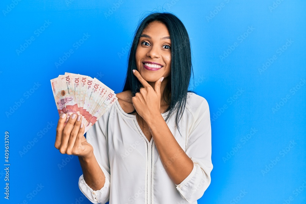 Young african american woman holding 10 colombian pesos banknotes looking confident at the camera smiling with crossed arms and hand raised on chin. thinking positive. Young african american woman holding 10 colombian pesos banknotes looking confident at the camera smiling with crossed arms and hand raised on chin. thinking positive.