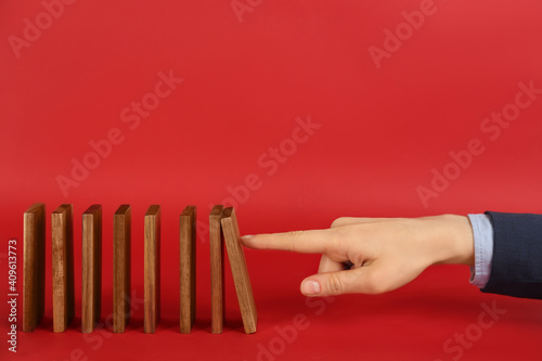Woman causing chain reaction by pushing domino tile on red background, closeup. Space for text