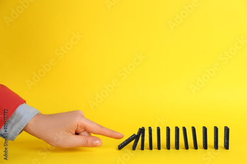 Woman causing chain reaction by pushing domino tile on yellow background, closeup. Space for text photo