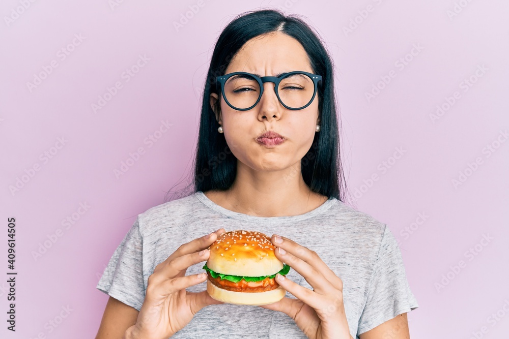 Beautiful young woman eating tasty hamburger puffing cheeks with funny face. mouth inflated with air, catching air. Beautiful young woman eating tasty hamburger puffing cheeks with funny face. mouth inflated with air, catching air.