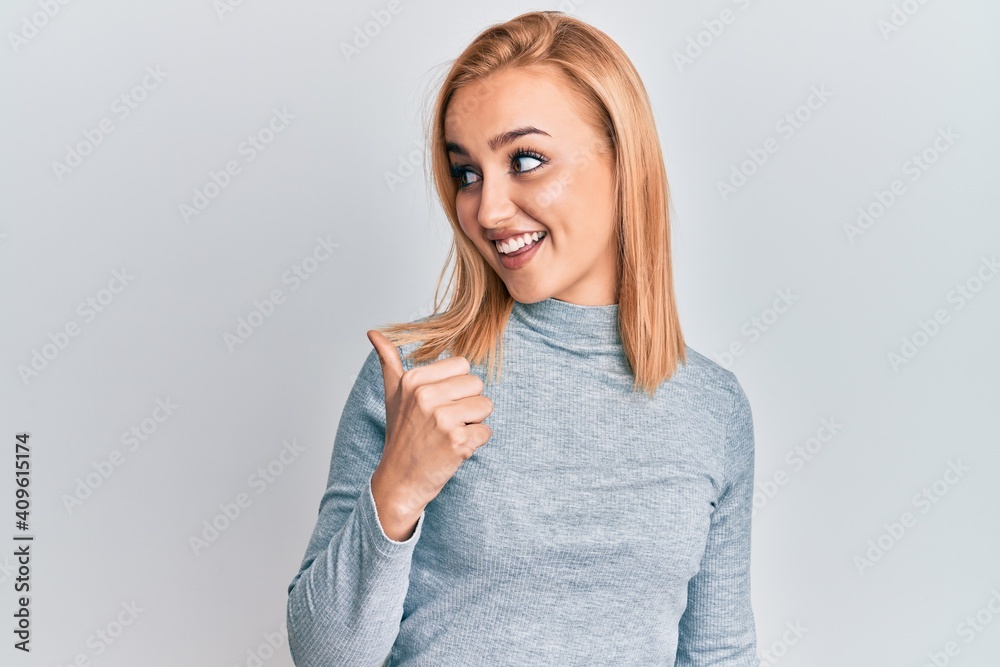 Beautiful caucasian woman wearing casual clothes pointing thumb up to the side smiling happy with open mouth Beautiful caucasian woman wearing casual clothes pointing thumb up to the side smiling happy with open mouth