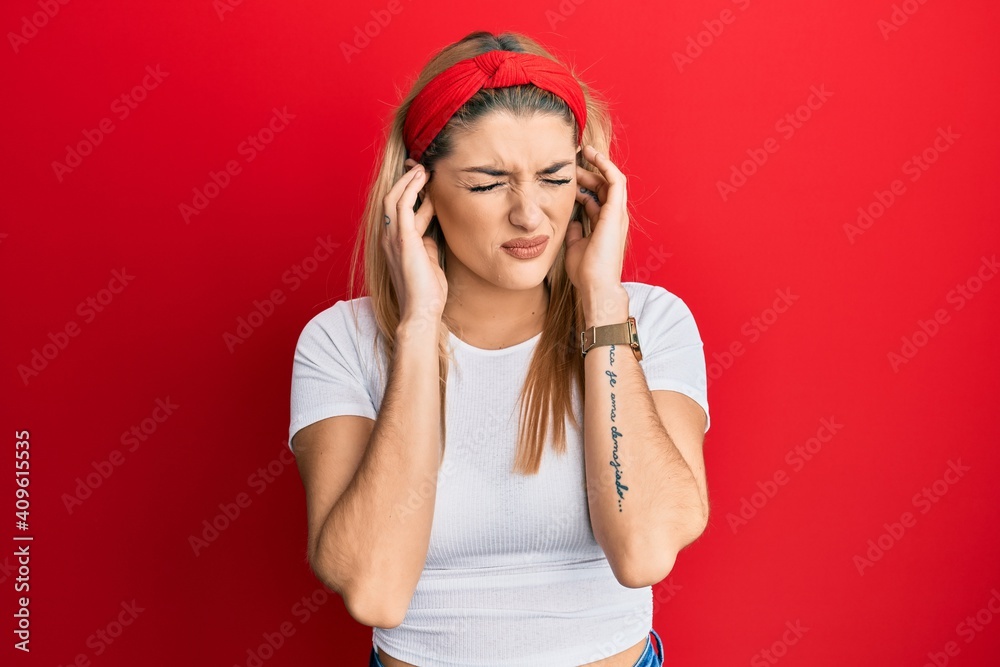 Young caucasian woman wearing casual white t shirt covering ears with fingers with annoyed expression for the noise of loud music. deaf concept. Young caucasian woman wearing casual white t shirt covering ears with fingers with annoyed expression for the noise of loud music. deaf concept.
