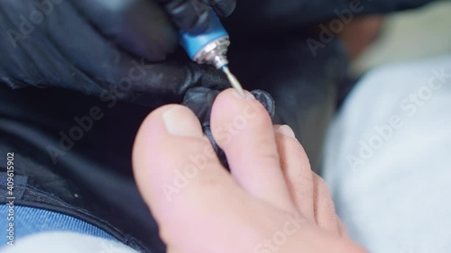 Beauty master pedicures man's toes using electical hardwear manicure machine. Close up view of right foot
