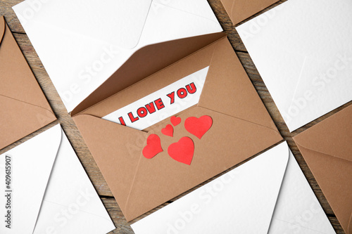 Sheet of paper with phrase I Love You, envelopes and red hearts on wooden table, flat lay