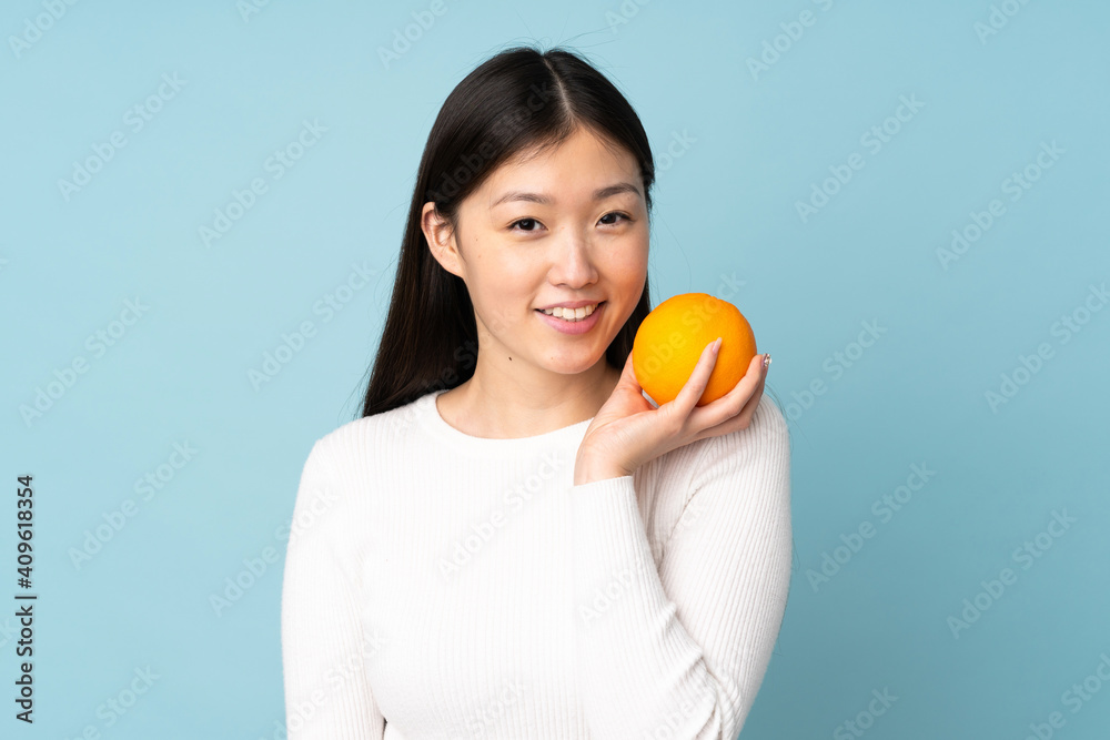 Young asian woman holding an orange over isolated blue background Young asian woman holding an orange over isolated blue background