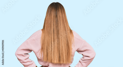 Beautiful blonde woman wearing casual winter pink sweater standing backwards looking away with arms on body