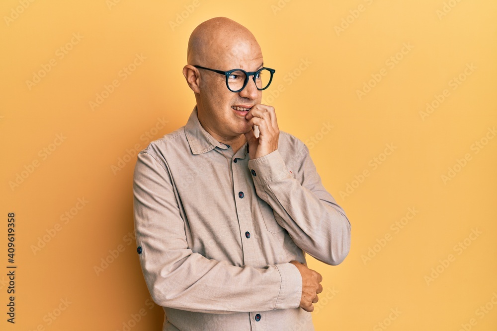 Middle age bald man wearing casual clothes and glasses looking stressed and nervous with hands on mouth biting nails. anxiety problem. Middle age bald man wearing casual clothes and glasses looking stressed and nervous with hands on mouth biting nails. anxiety problem.