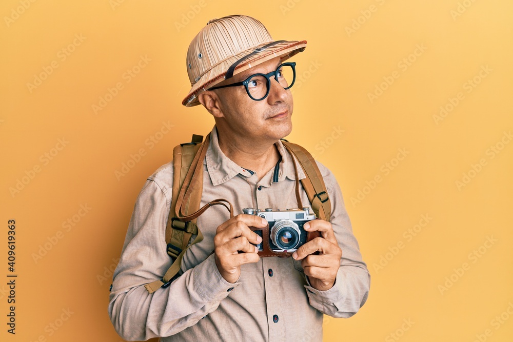 Middle age bald man wearing explorer hat and vintage camera smiling looking to the side and staring away thinking. Middle age bald man wearing explorer hat and vintage camera smiling looking to the side and staring away thinking.