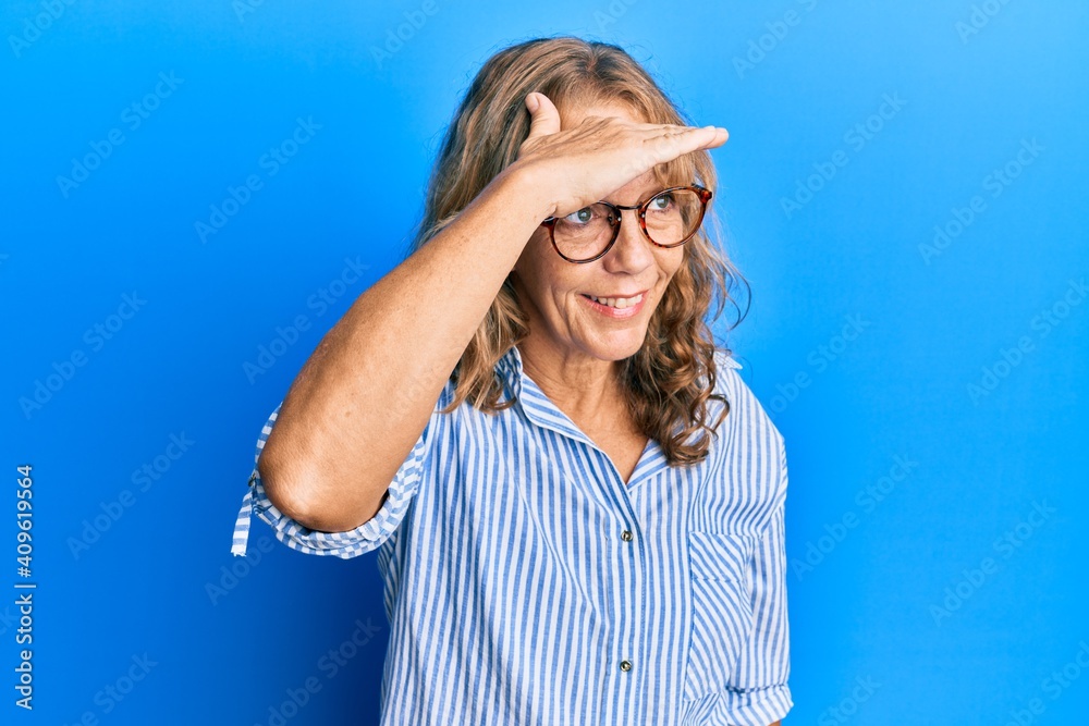 Middle age blonde woman wearing casual clothes and glasses very happy and smiling looking far away with hand over head. searching concept. Middle age blonde woman wearing casual clothes and glasses very happy and smiling looking far away with hand over head. searching concept.