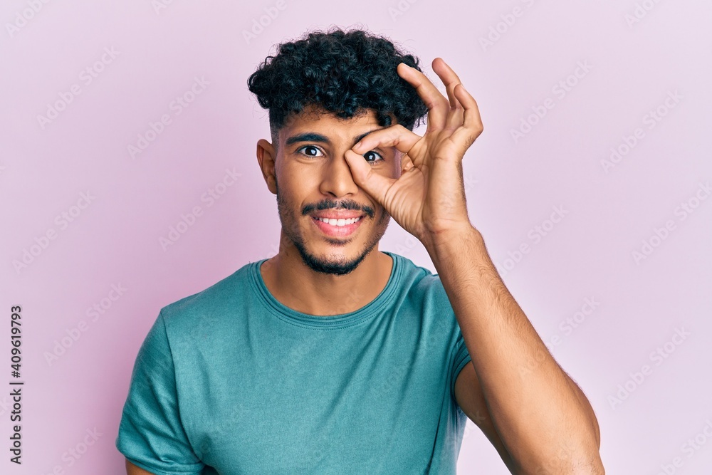 Young arab handsome man wearing casual clothes doing ok gesture with hand smiling, eye looking through fingers with happy face. Young arab handsome man wearing casual clothes doing ok gesture with hand smiling, eye looking through fingers with happy face.