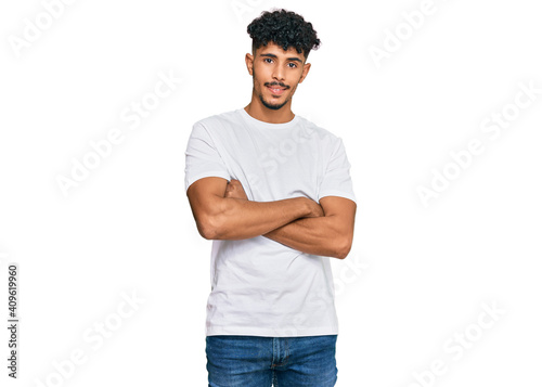 Young arab man wearing casual white t shirt happy face smiling with crossed arms looking at the camera. positive person.