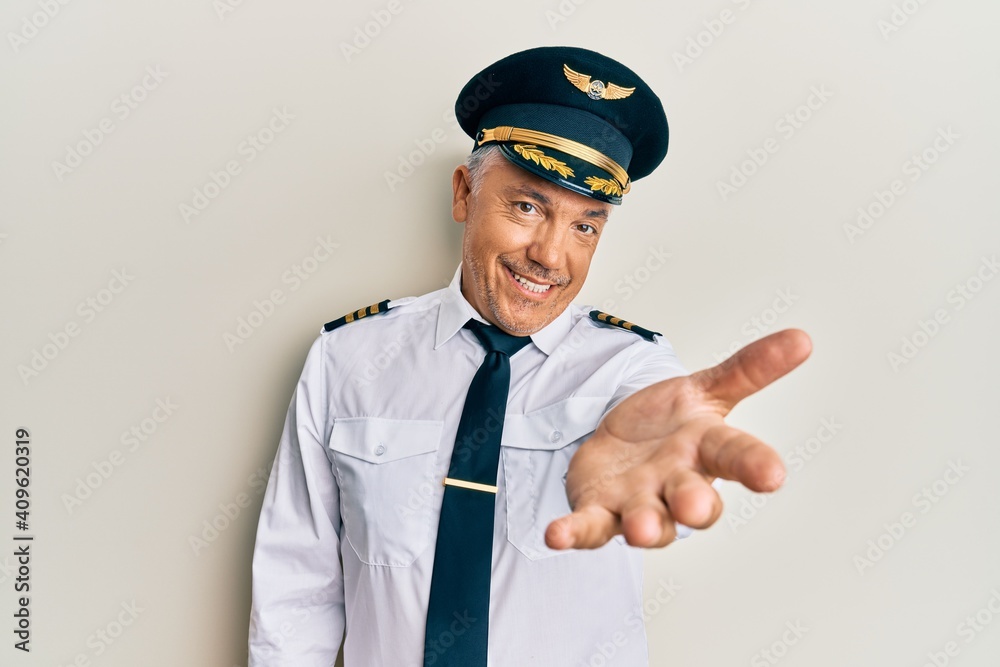 Handsome middle age mature man wearing airplane pilot uniform smiling cheerful offering palm hand giving assistance and acceptance. Handsome middle age mature man wearing airplane pilot uniform smiling cheerful offering palm hand giving assistance and acceptance.