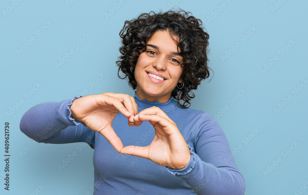 Young hispanic woman with curly hair wearing casual clothes smiling in love doing heart symbol shape with hands. romantic concept. Young hispanic woman with curly hair wearing casual clothes smiling in love doing heart symbol shape with hands. romantic concept.