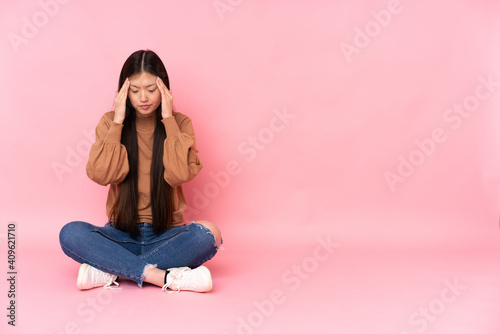 Young asian woman sitting on the floor isolated on pink background with headache © luismolinero