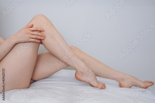 Woman body care. Close up of long female tanned legs with perfect smooth soft skin, pedicure, healthy nails on white medical couch and background. Epilation, beauty and health concept.