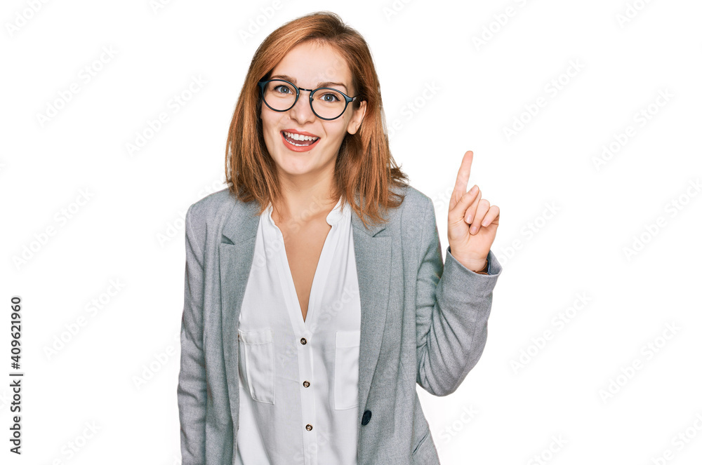 Young caucasian woman wearing business style and glasses pointing finger up with successful idea. exited and happy. number one. Young caucasian woman wearing business style and glasses pointing finger up with successful idea. exited and happy. number one.