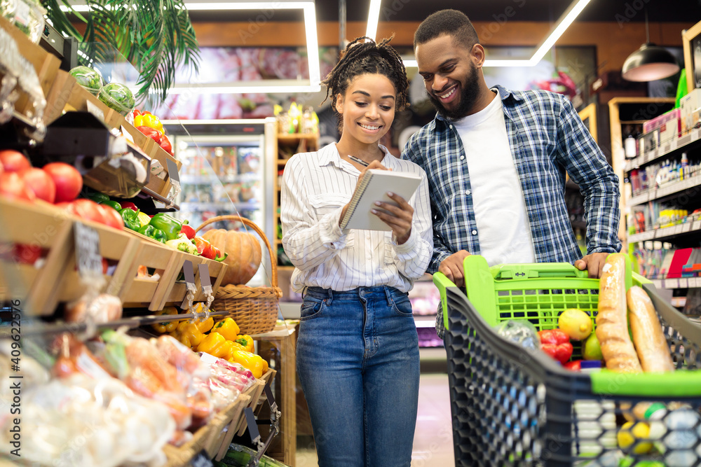 Black Family Buying Food Taking Notes In Checklist In Supermarket