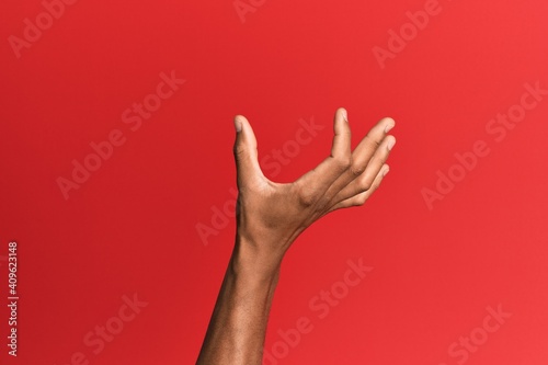 Wall Mural Hand of hispanic man over red isolated background picking and taking invisible t