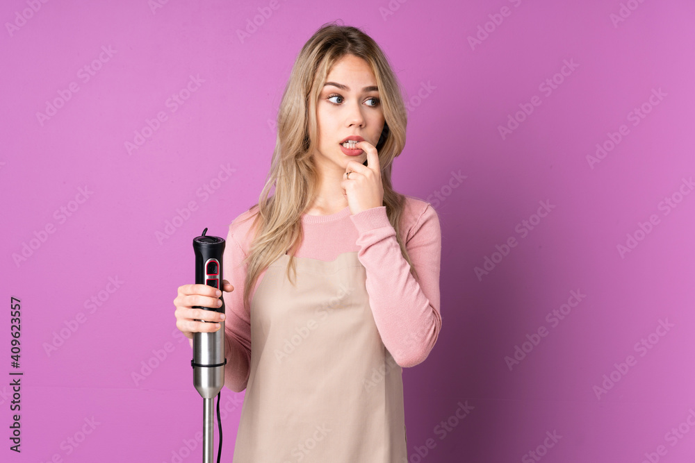 Teenager Russian girl using hand blender isolated on purple background nervous and scared Teenager Russian girl using hand blender isolated on purple background nervous and scared
