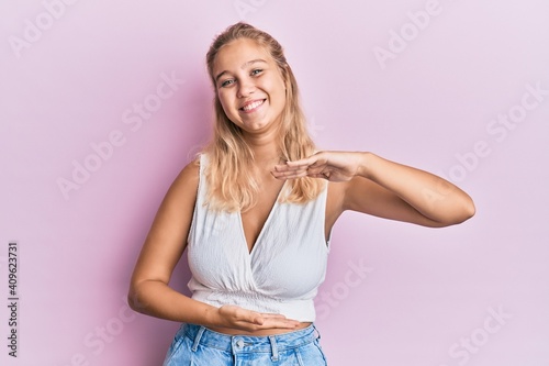 Young blonde girl wearing casual clothes gesturing with hands showing big and large size sign  measure symbol. smiling looking at the camera. measuring concept.
